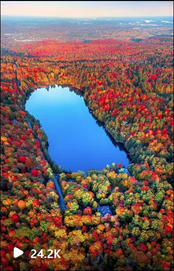 an aerial view of a lake surrounded by trees with Fall color leaves in Gatineau park 